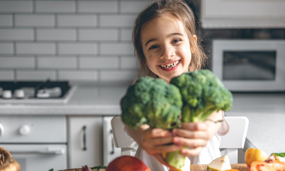 Happy girl holding up broccoli